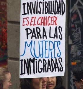 A woman holds a sign during a Barcelona demonstration on International Women's Day in 2009. The sign reads "Invisibility is the cancer for immigrant women." (Wikimedia Commons)