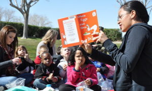 Taimane Mejia, a volunteer at McTureous Hall aboard Marine Corps Logistics Base Barstow, reads to children from the Child Development Center for the annual Dr. Seuss Birthday Bash, March 2, 2012. During the event, children had stories read to them to help stress the importance of literacy at all ages and participated in other activities such as coloring and games. (United States Marine Corp via Wikimedia Commons)